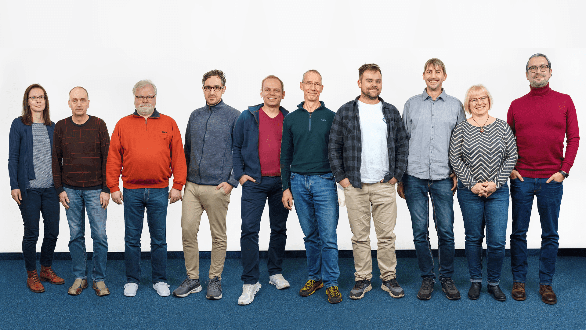 Eleven diverse team members stand together smiling against a plain white background.