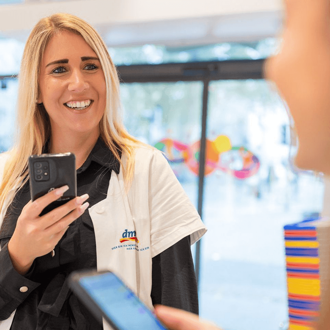 Smiling blonde woman in lab coat holding a phone during a mobile payment transaction.