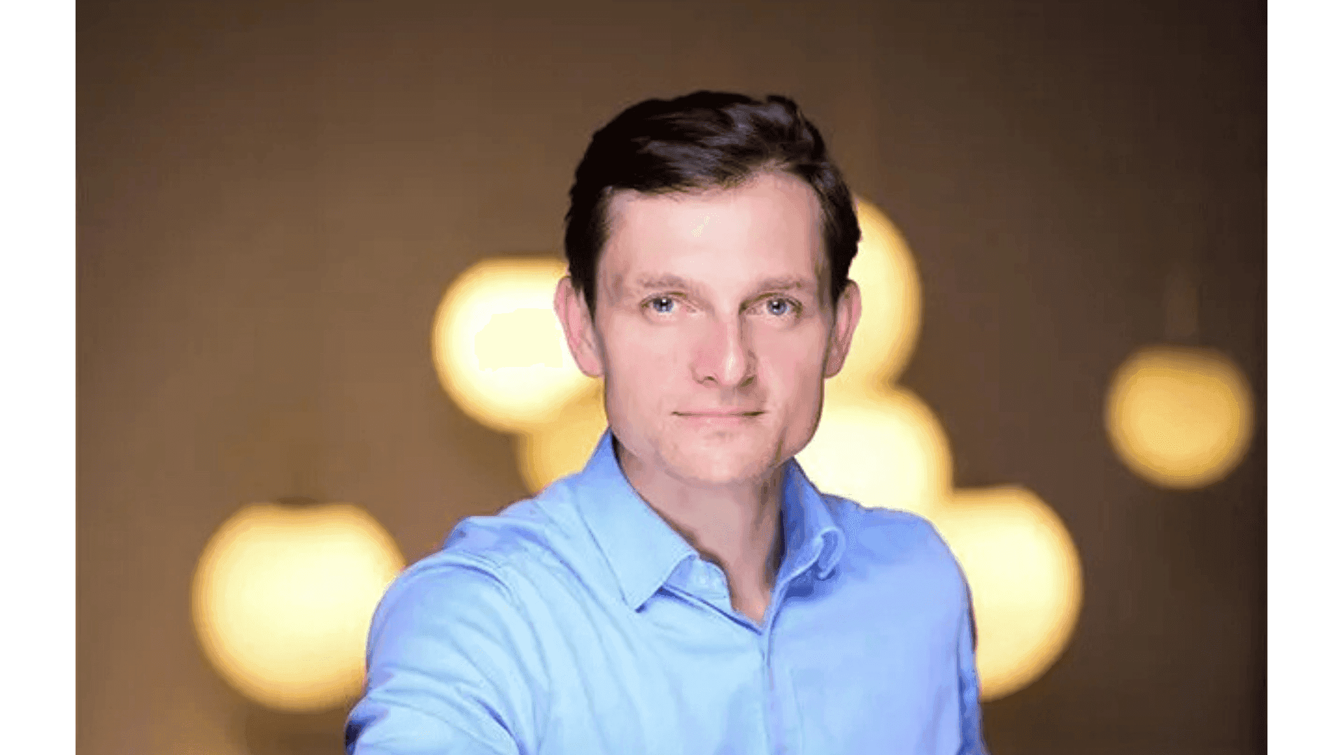 Professional man in a blue shirt with a warm, blurred background looking at the camera.